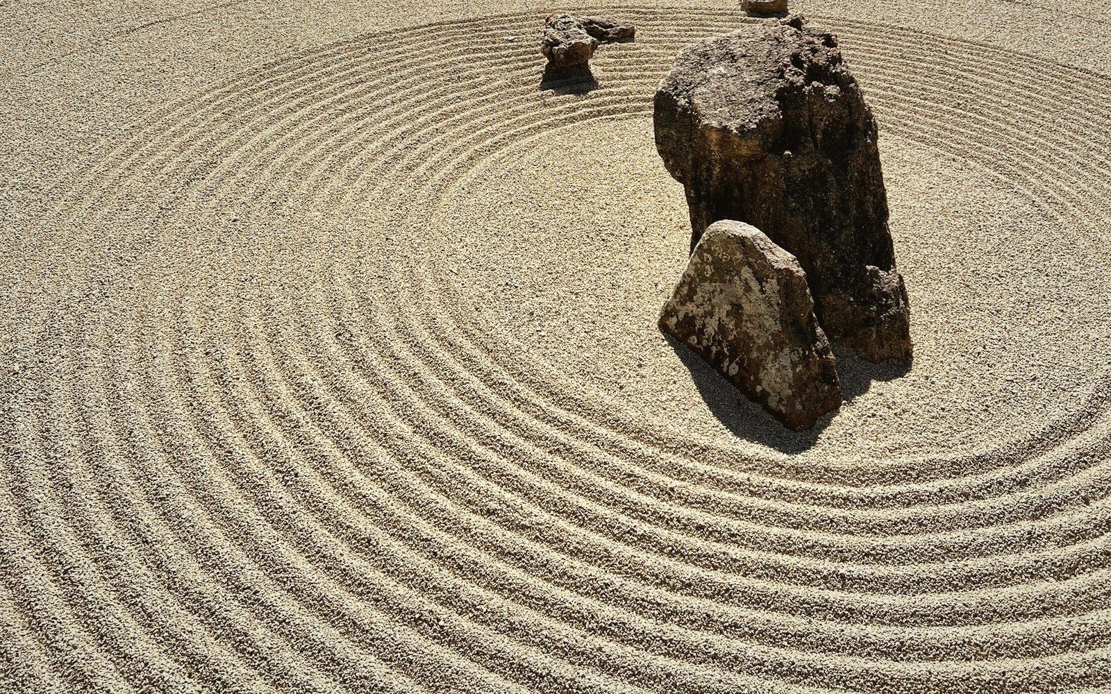 Concentric raked gravel patterns curve around clustered rocks in a zen garden